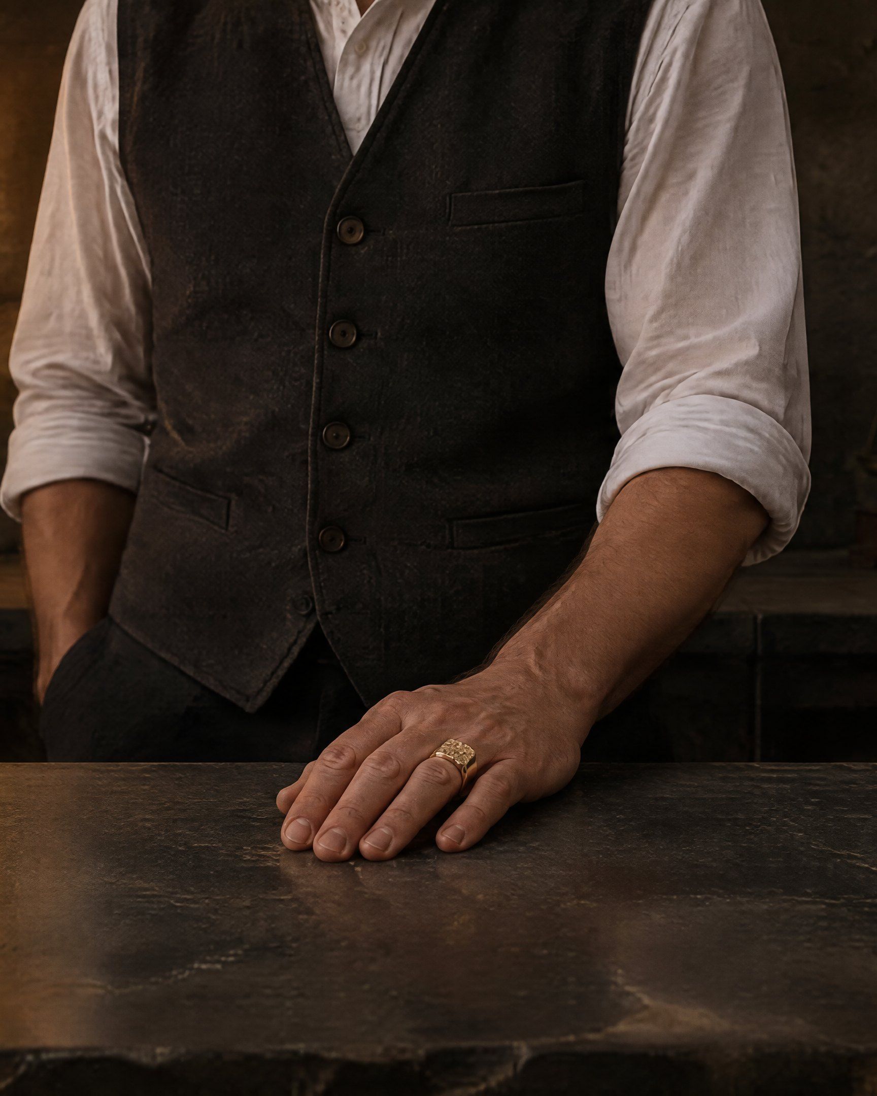 A hand on a dark stone counter under a bare tungsten bulb, wearing the No. 502 Bullion nugget ring in 14K yellow gold