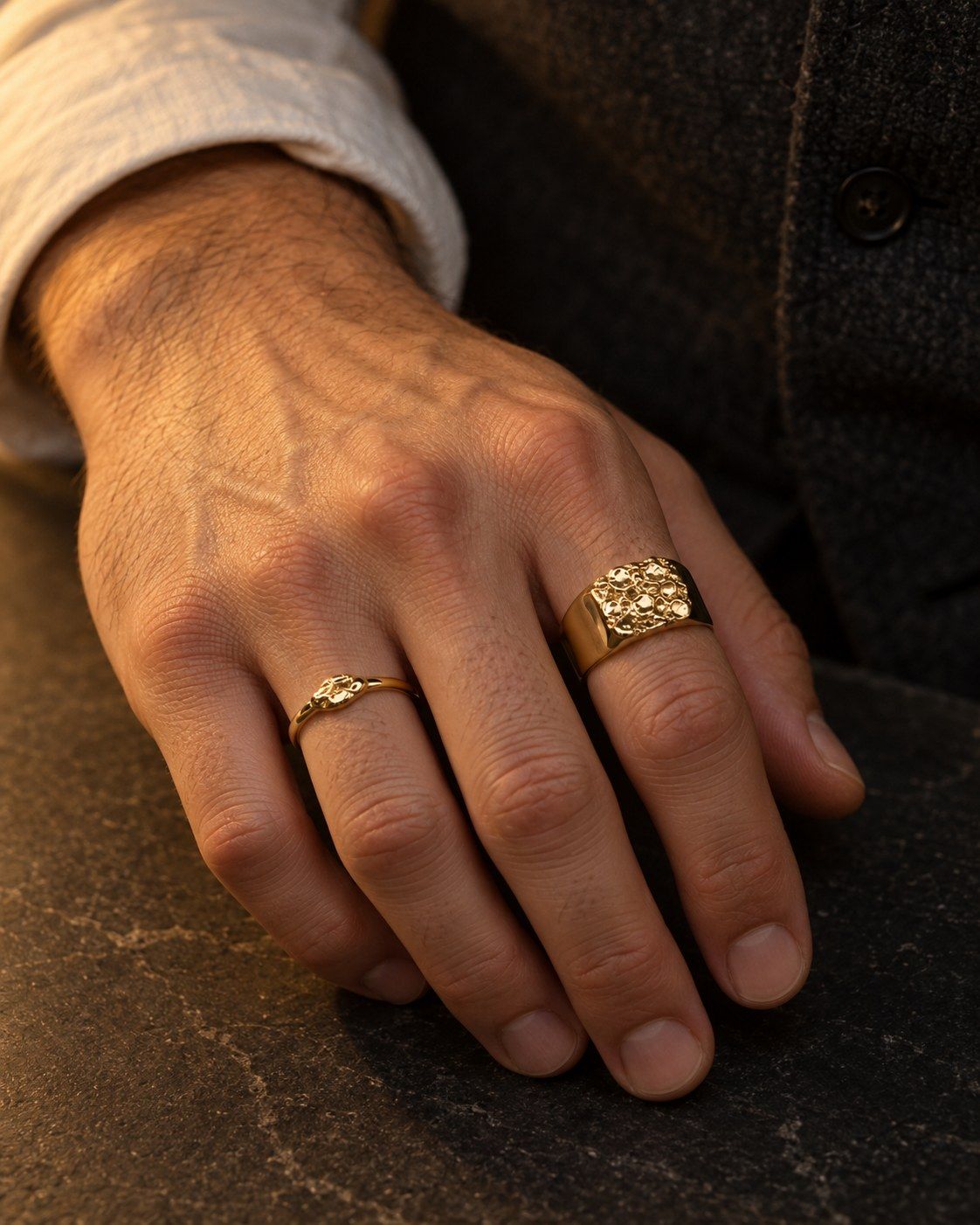 A hand on a dark slate counter wearing No. 502 Bullion and No. 525 Grain, 14K yellow gold