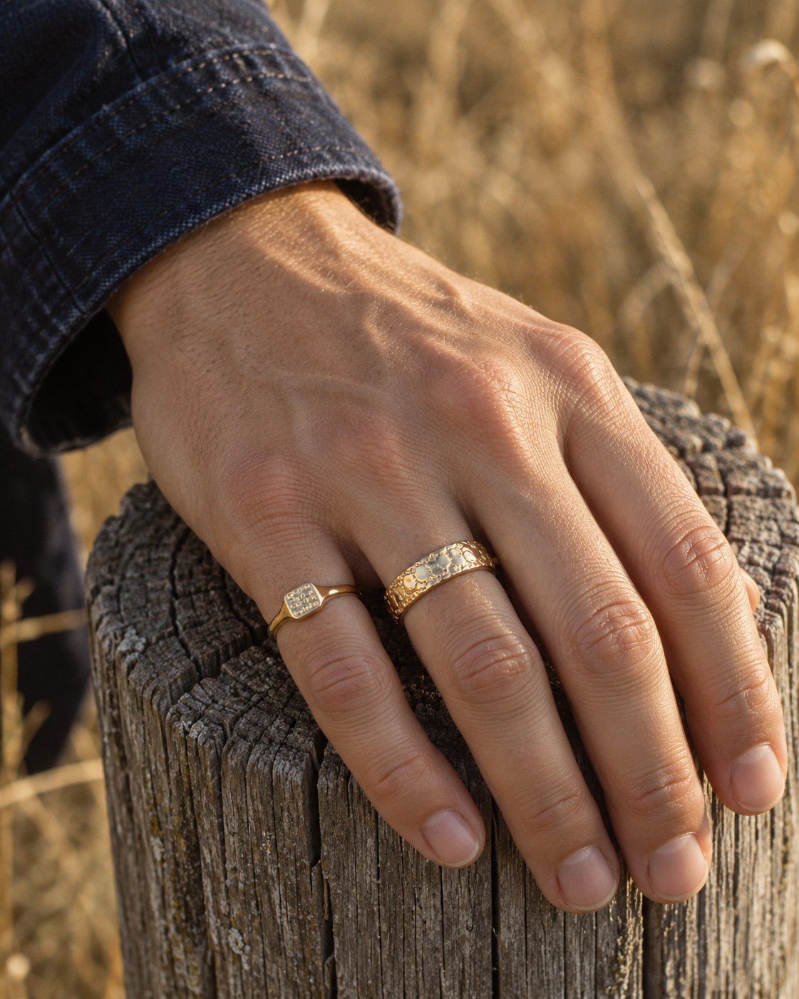 A hand on a weathered timber post wearing No. 446 Signet XS and No. 441 Nugget Band 6 mm, 14K yellow gold
