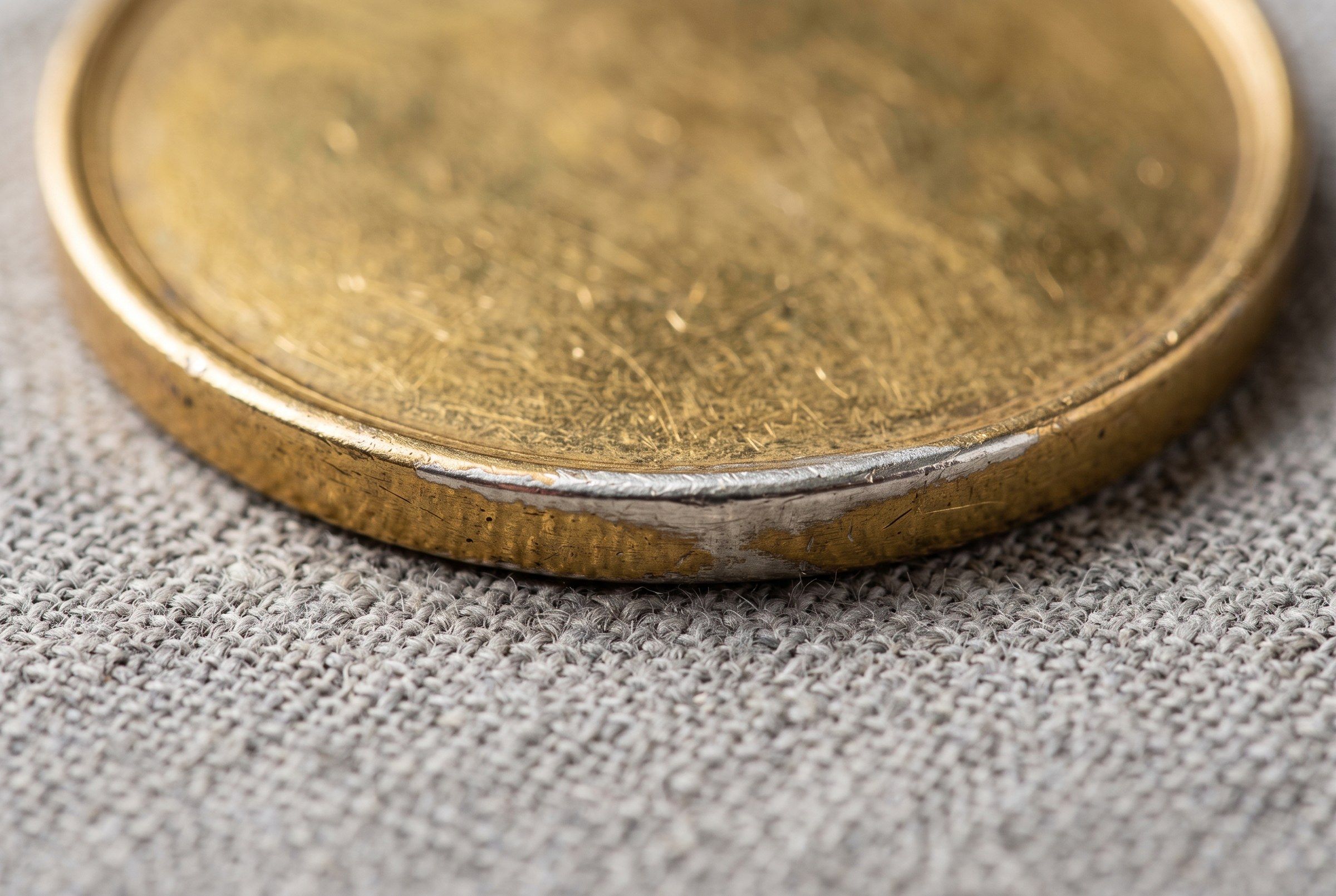 Close-up of the worn rim of a gold-colored medal where the thin gold coat has rubbed through to bright silver underneath