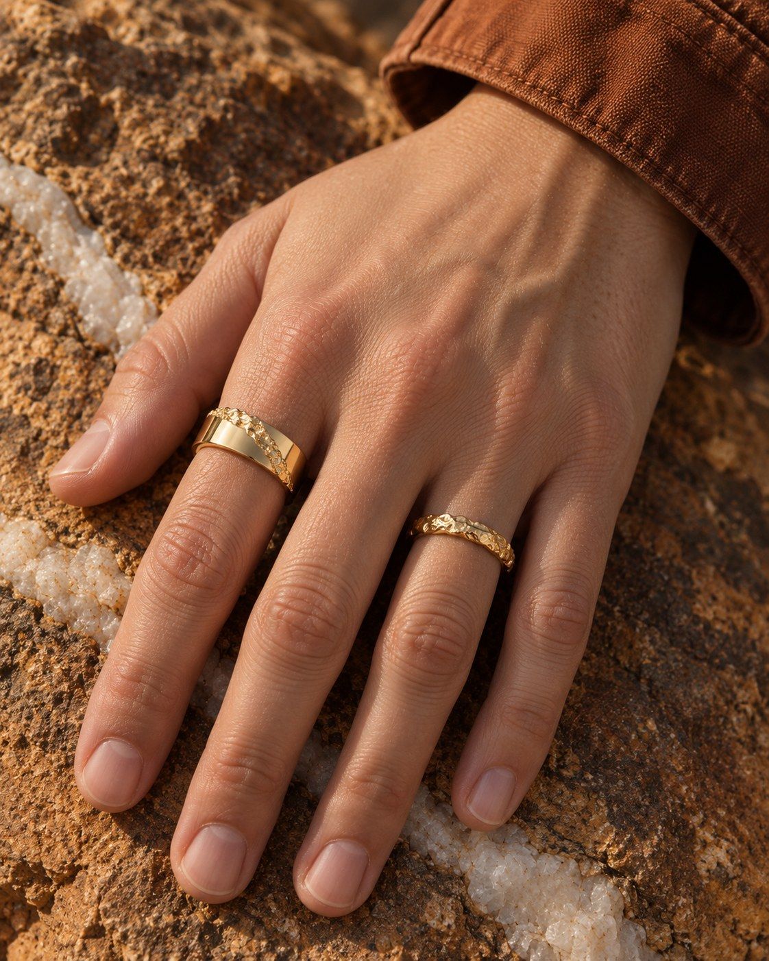A hand on ochre rock wearing No. 518 Fault Line and No. 024 Slim, 14K yellow gold