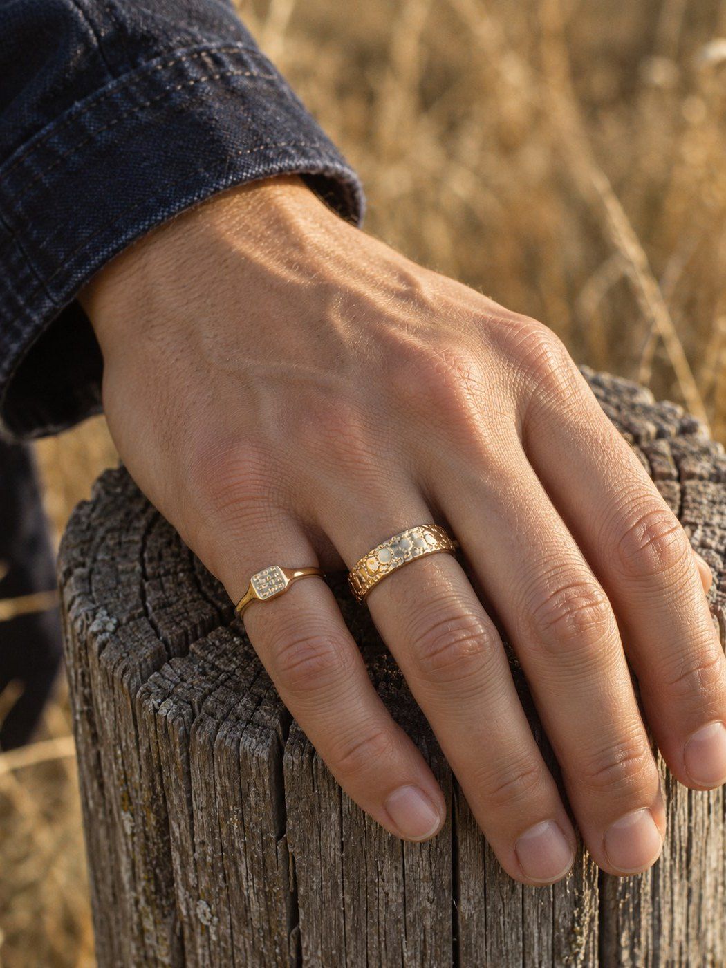 Signet XS No. 446 and Nugget Band 6 mm No. 441 in solid 14K gold, together on one hand on a weathered timber post