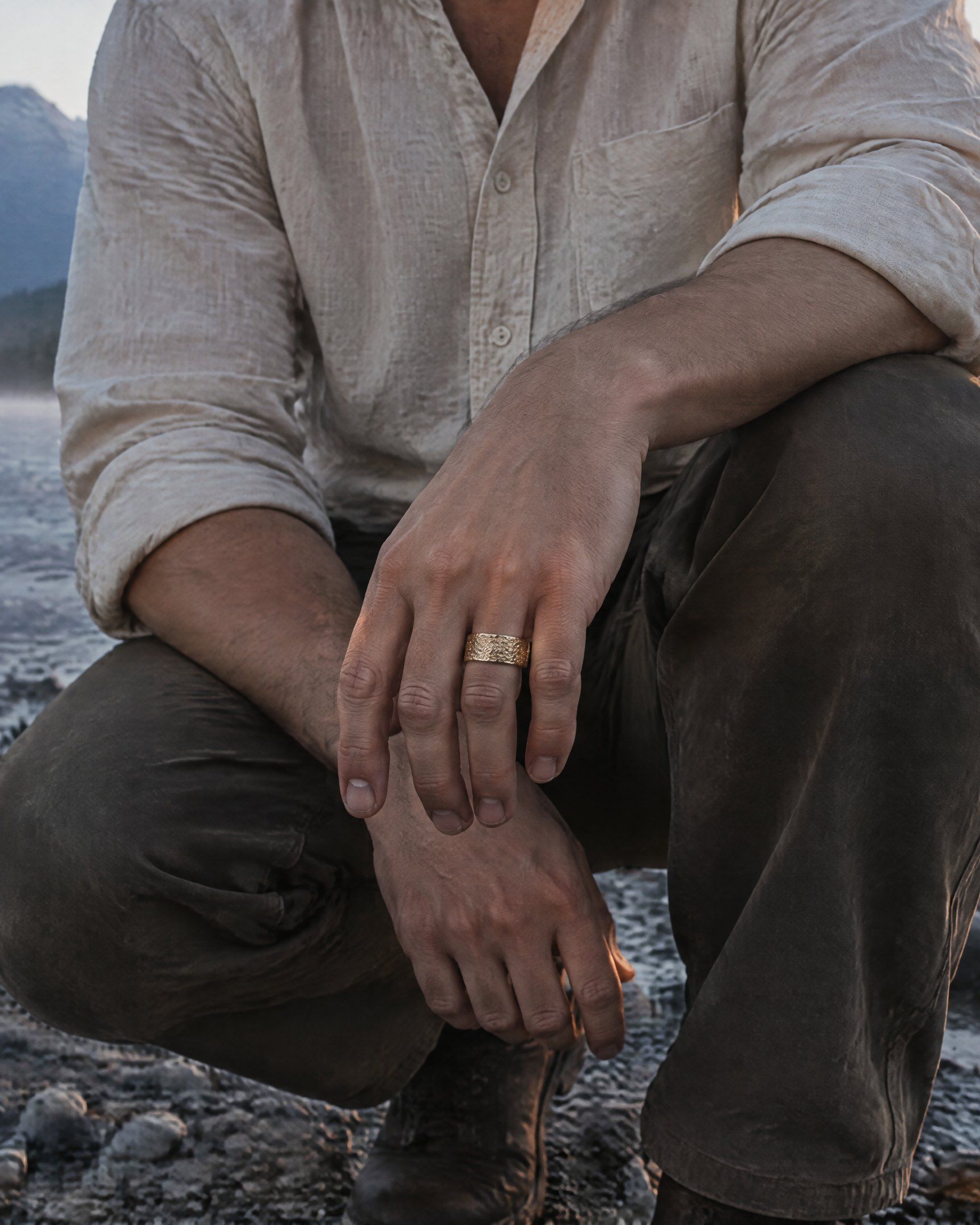 Someone crouched at the edge of a creek at dawn, wearing the No. 508 Placer nugget ring in 14K yellow gold
