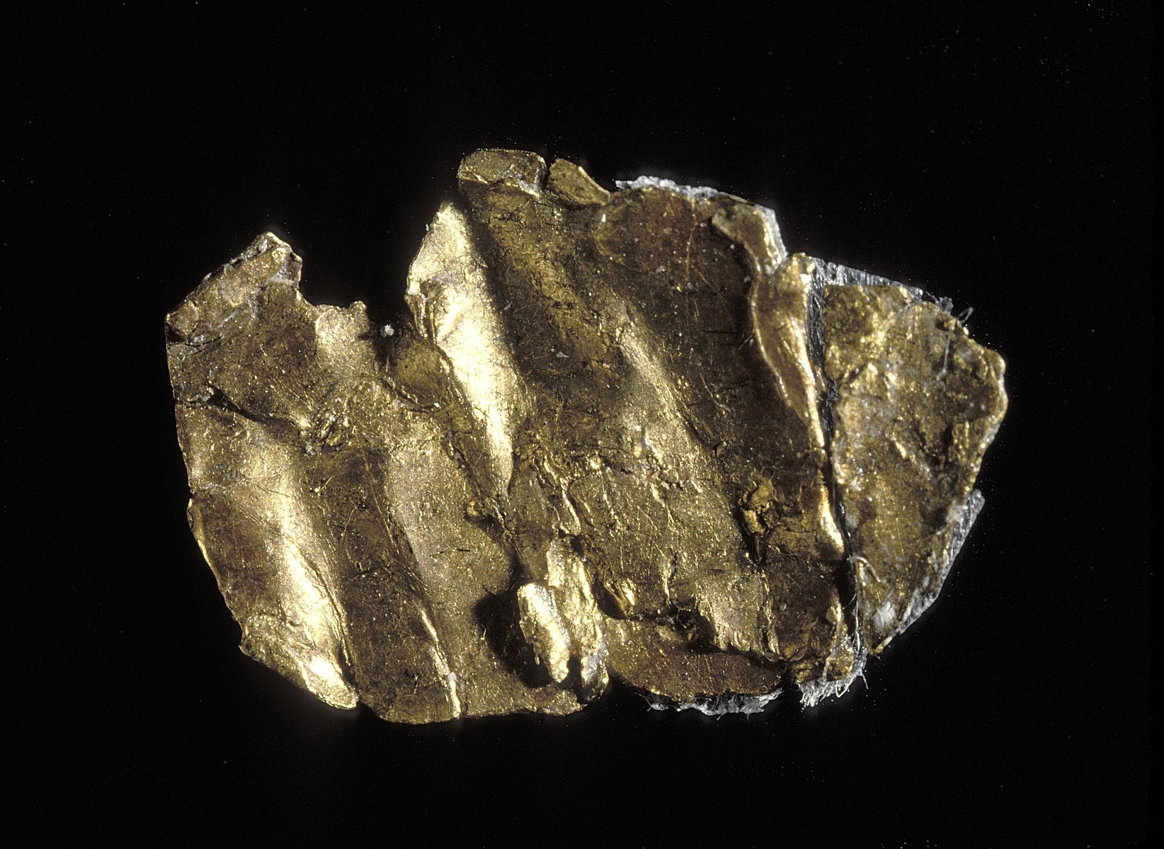 A small flat piece of natural gold, folded and scratched, on a black background